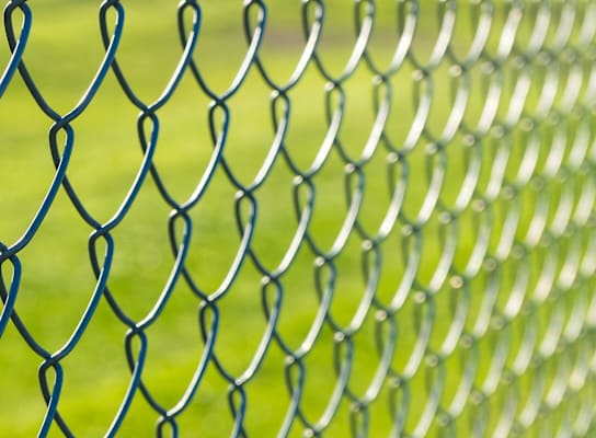 a close up of a chain link fence with a field of grass behind it