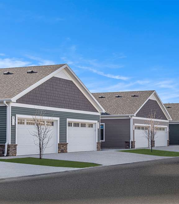 A row of ducks are walking in front of a house.