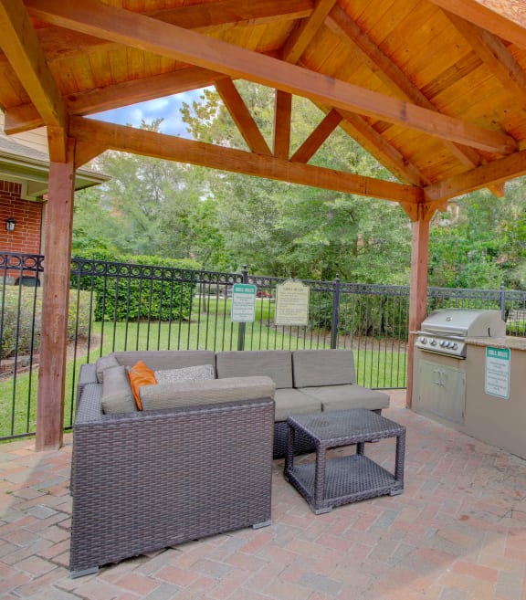 an outdoor kitchen with a grill and a seating area under a wooden awning