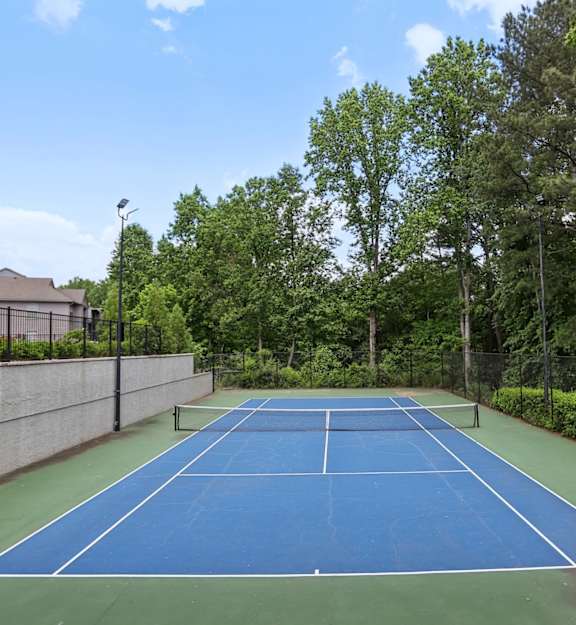 a blue tennis court with a fence and trees