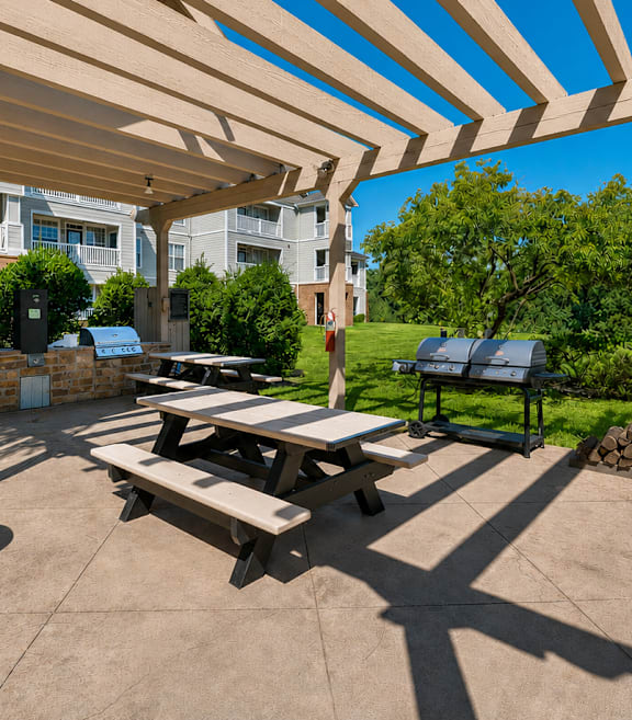 A patio with a grill and picnic table under a wooden pergola.