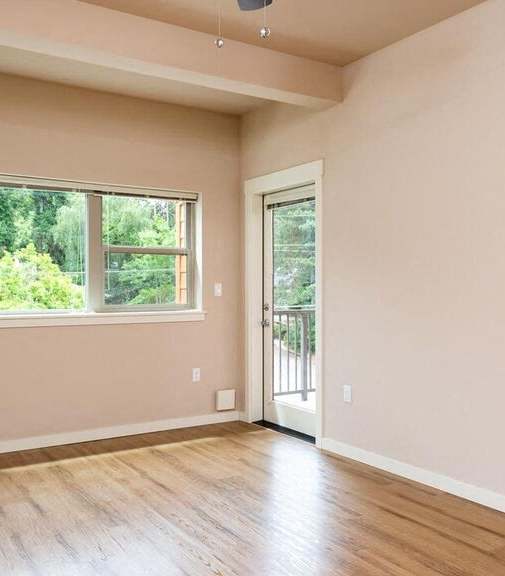 an empty living room with a large window and wooden floors