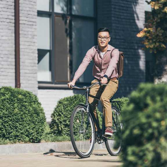 A man in a pink shirt and khaki pants is riding a bicycle on a sidewalk.