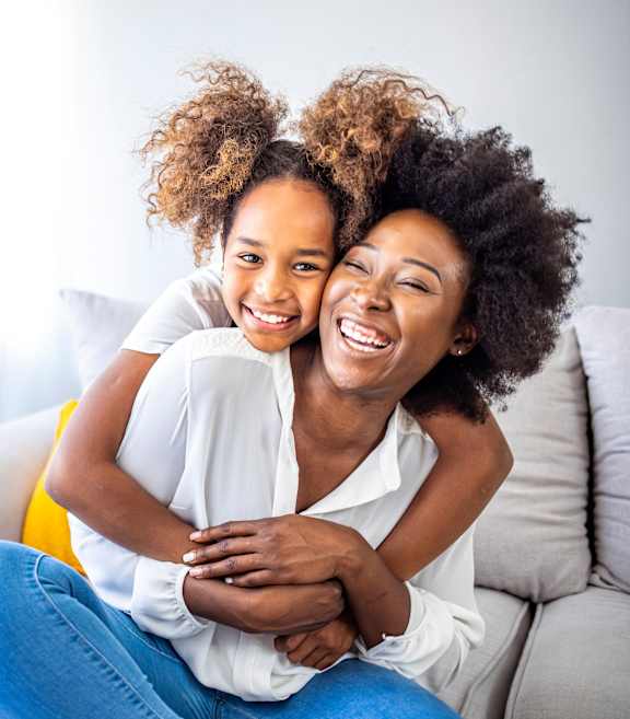 A woman and a young girl are sitting on a couch, sharing a joyful moment.