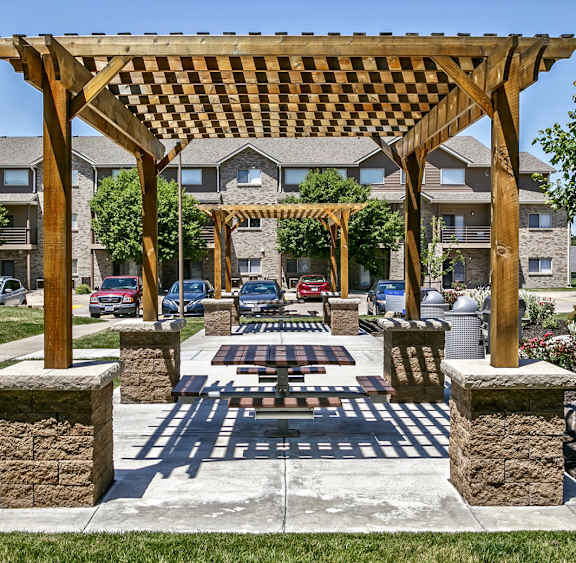 A wooden pergola structure is situated in a grassy area with stone pillars.