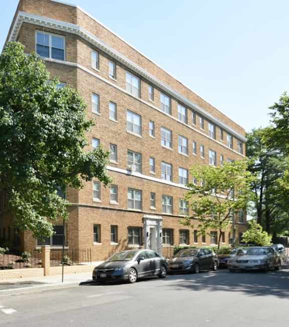 A street view of a row of parked cars in front of a brick building.