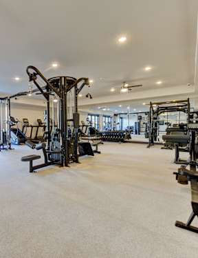 A spacious gym with a variety of equipment including treadmills, weights, and a ceiling fan.