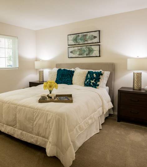 A bedroom with a bed, nightstand, and a plant.