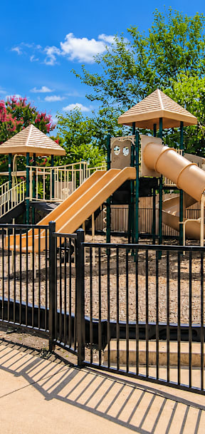 A playground with a yellow slide and a black fence.