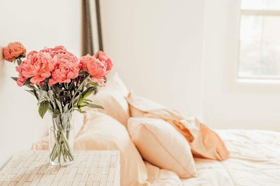 A bouquet of pink flowers sits on a table in front of a bed.