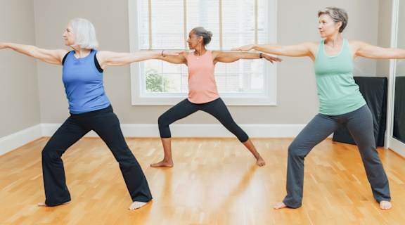 Three women are practicing yoga in a room with wooden floors.