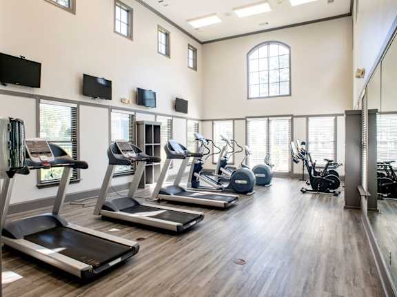 A spacious gym with treadmills, exercise bikes, and television screens mounted on the wall.