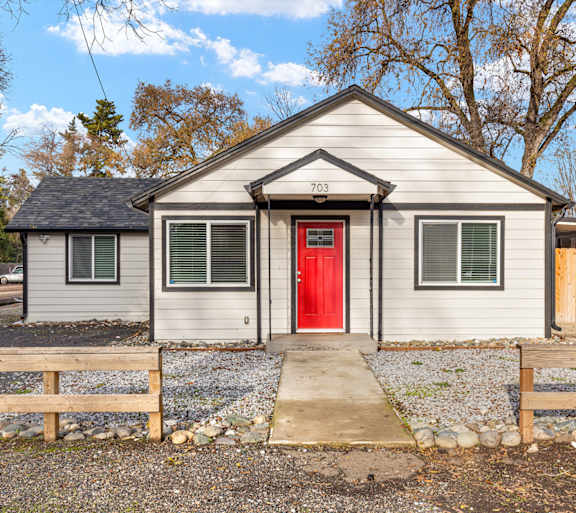 A small house with a red door is surrounded by a gravel area and wooden fences.