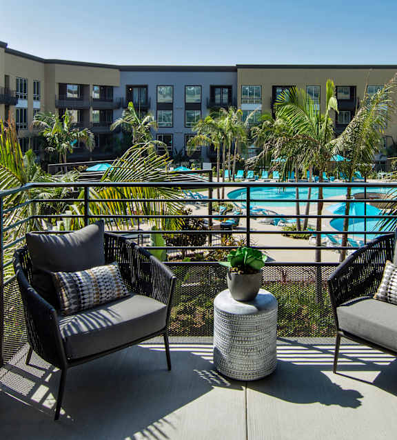 Two chairs are on a balcony overlooking a pool.