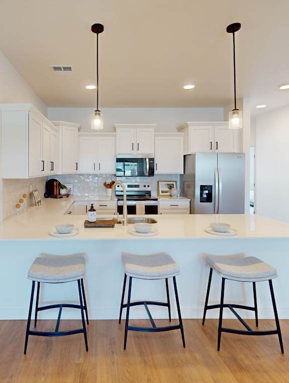 A kitchen with white cabinets and a white island with three bar stools.