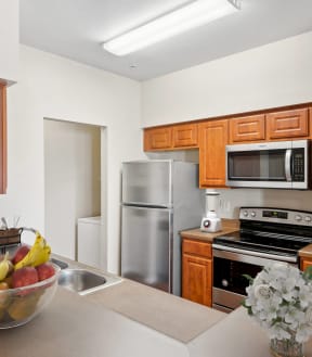 a kitchen with brown cabinets and black and silver appliances and a fruit bowl and flowers on the counter