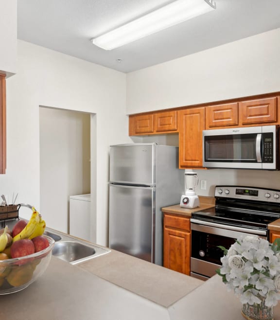 a kitchen with brown cabinets and black and silver appliances and a fruit bowl and flowers on the counter at Cypress Gardens, Cedar Park, TX, 78613