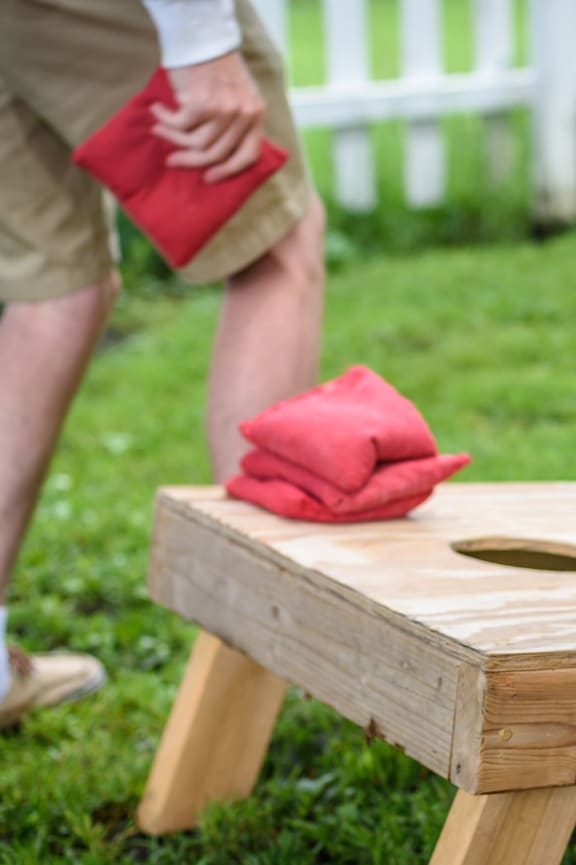 A man is playing cornhole with a red bag of chips.