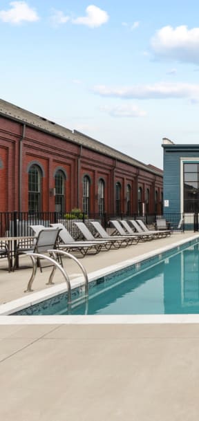 a swimming pool with lounge chairs and umbrellas in front of a brick building