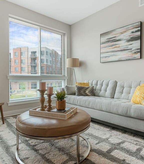 A living room with a grey couch, a wooden chair, a coffee table, and a large window.