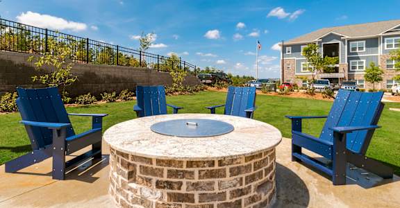 A fire pit surrounded by blue chairs in a sunny outdoor setting.