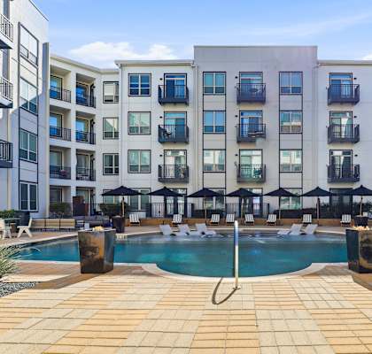 A swimming pool surrounded by a tiled patio and apartment buildings.