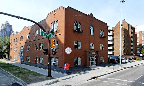 A street view of a residential area with apartment buildings on the right and a car driving on the road.