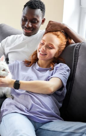 a man and a woman sitting on a couch holding a white cat