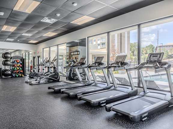 a large fitness room with cardio equipment and large windows