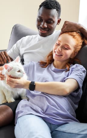 a man and a woman sitting on a couch holding a white cat