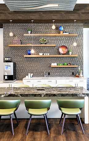 A modern kitchen with a marble countertop and green chairs.