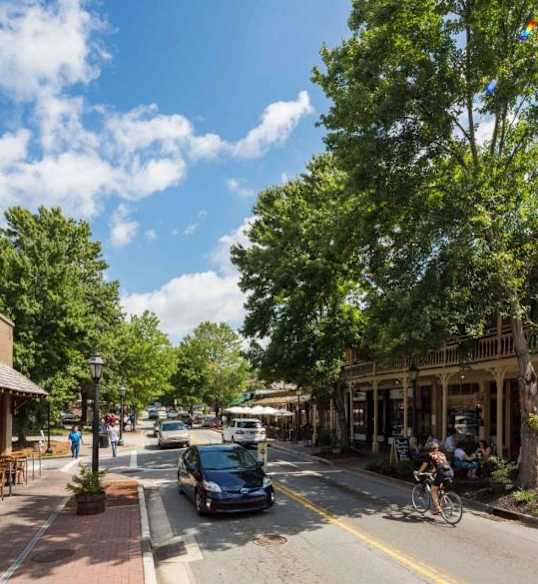 A street view of a small town with people sitting at outdoor tables.