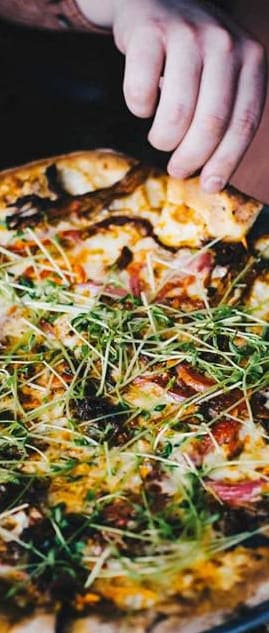 a person reaching for a pizza on a table