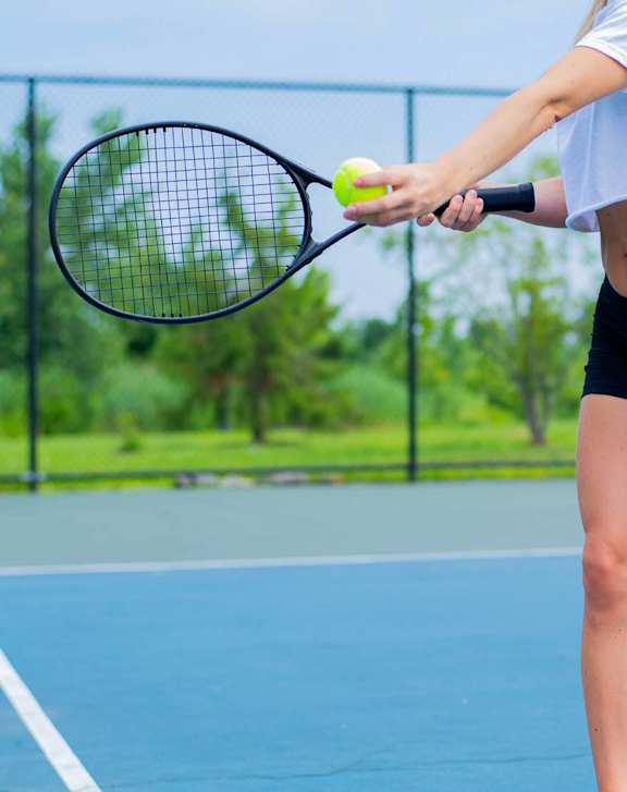A woman in a white top and black shorts is playing tennis on a blue court.