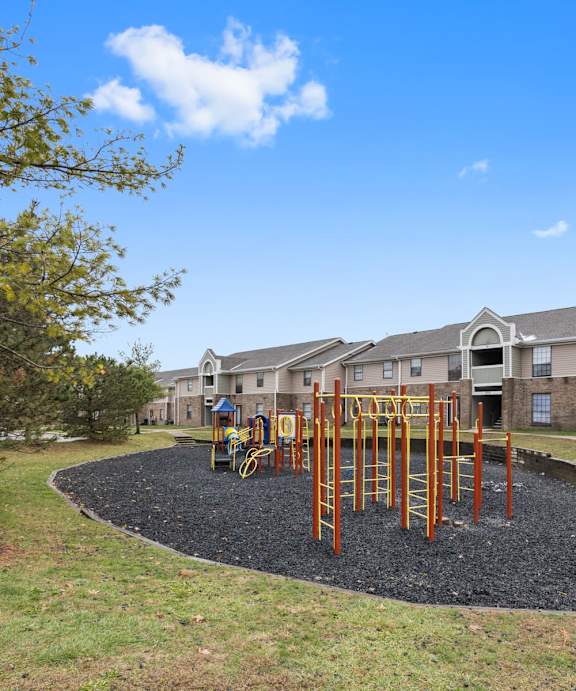 A playground with a swing set in the middle of a gravel area in front of apartment buildings.at Eagles Edge Apartments, Indianapolis, IN 462542