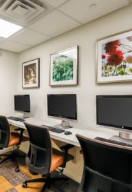 a computer room with three monitors on a table and chairs