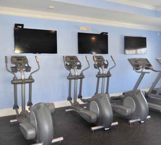 A gym with a row of exercise bikes and two flat screen TVs on the wall.