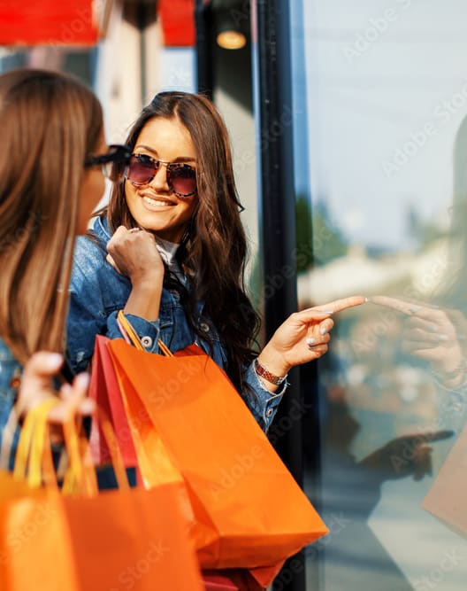Two women with shopping bags are looking at a shop window.