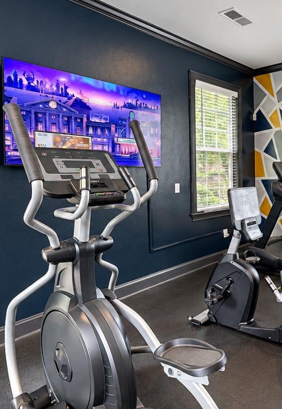 A gym with a variety of exercise equipment including treadmills, stationary bikes, and weight machines.
