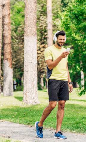 A man in a yellow shirt and blue shoes is walking on a path in a park.