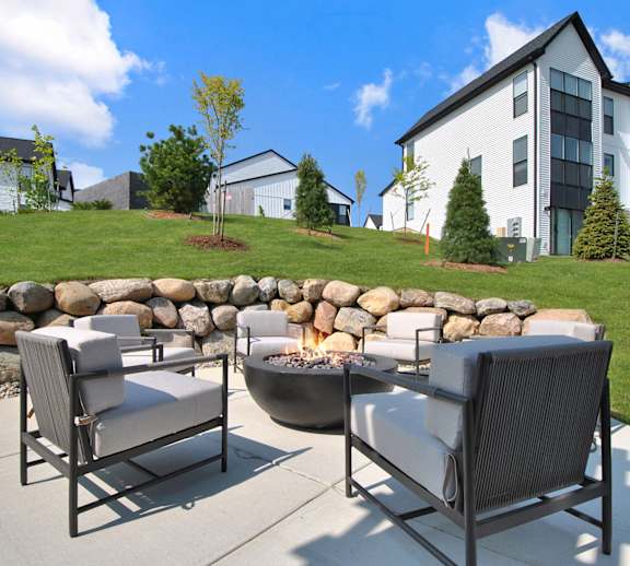 Two chairs are on a patio with a stone wall and a fire pit.