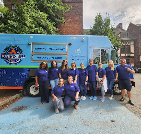 A group of people in blue shirts are standing in front of a blue food truck.
