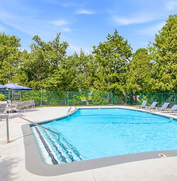 A swimming pool surrounded by a fence and chairs at Hidden Brook Apartment Homes Apartments, New Bedford, MA, 02740