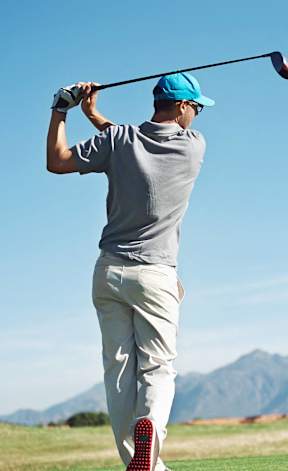 A man in a grey shirt and blue cap is playing golf on a sunny day.