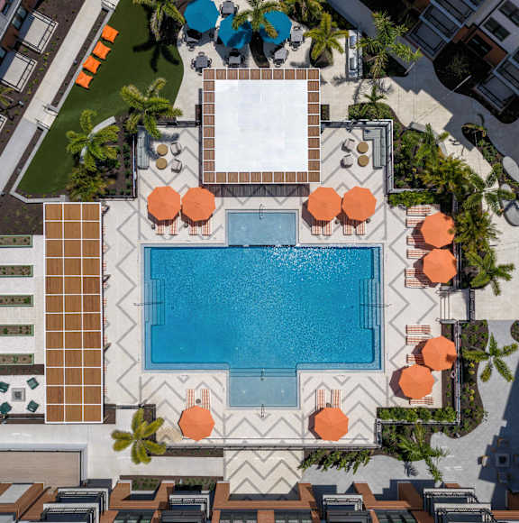 A pool surrounded by orange umbrellas and palm trees.