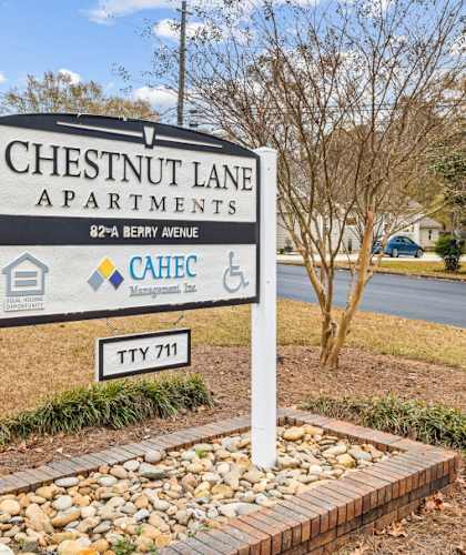 A sign for Chestnut Lane Apartments stands in front of a tree.