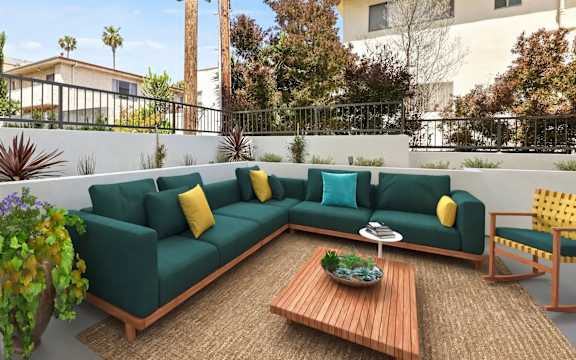 A green couch with yellow pillows is on a patio.