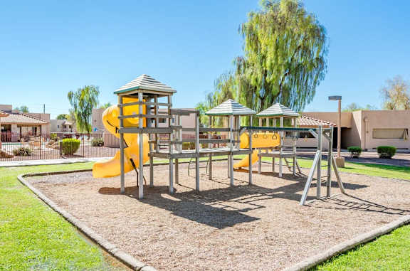 A playground with a yellow slide and a green lawn.