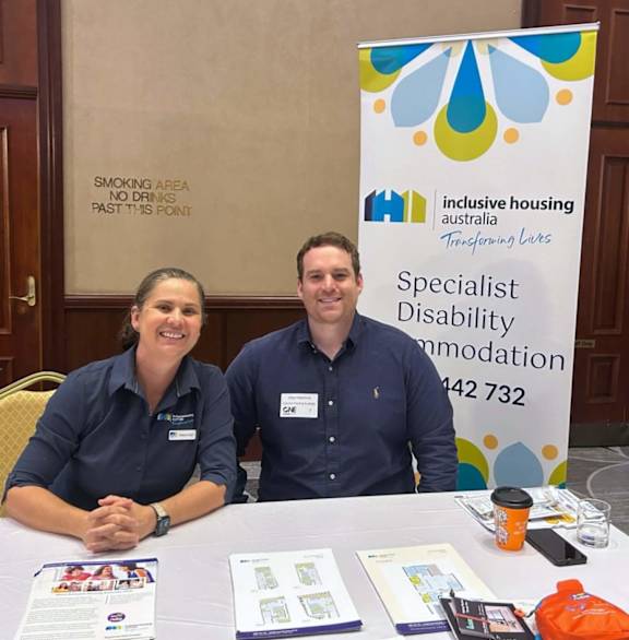 Two people sitting at a table with a sign that says "Specialist Disability Accommodation".