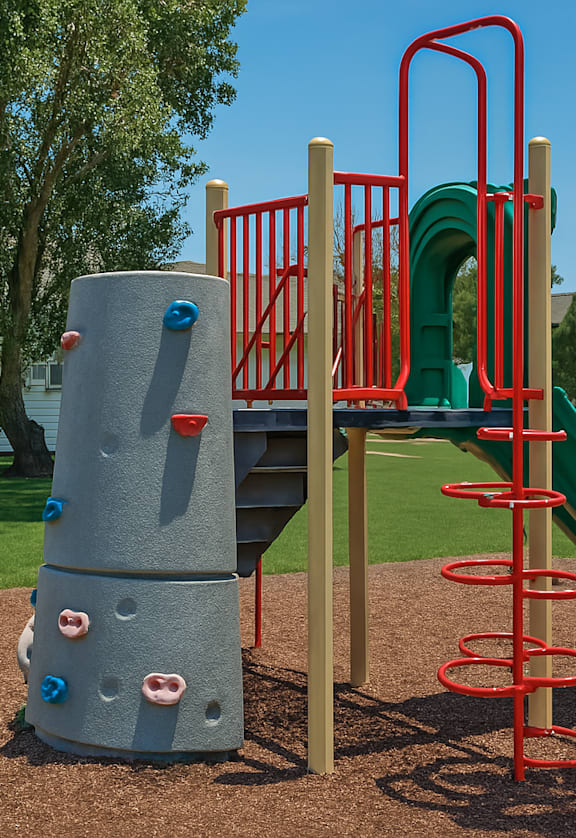 A playground with a green slide and a grey structure with red rings.